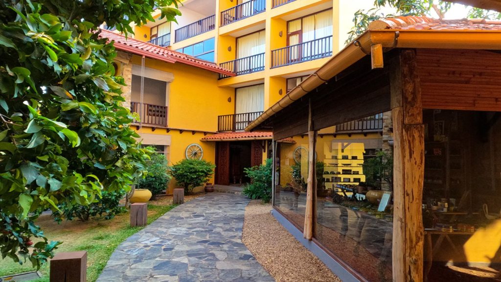 Außenbereich des Thaulle Resort in Sri Lanka mit gelbem Gebäude, Steinweg und tropischem Garten