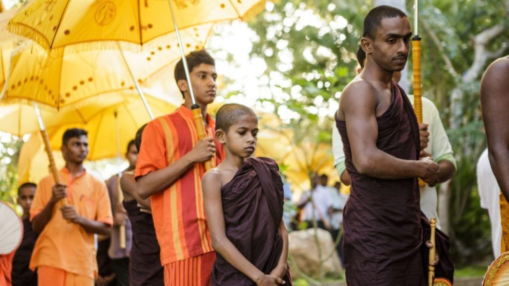 Buddhistische Prozession mit Mönchen, einem Kind und gelbem Schirm im warmen Tageslicht - Einweihung vom Thaulle Resort