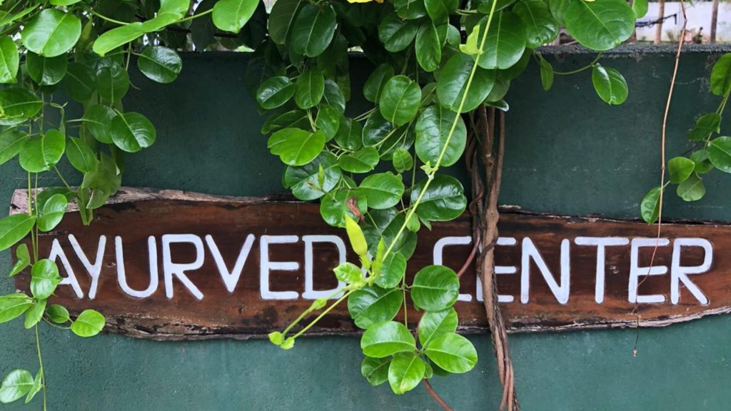 Schild des Ayurveda Centers vom Thaulle Resort Sri Lanka eingerahmt von grünen Blättern und tropischer Vegetation