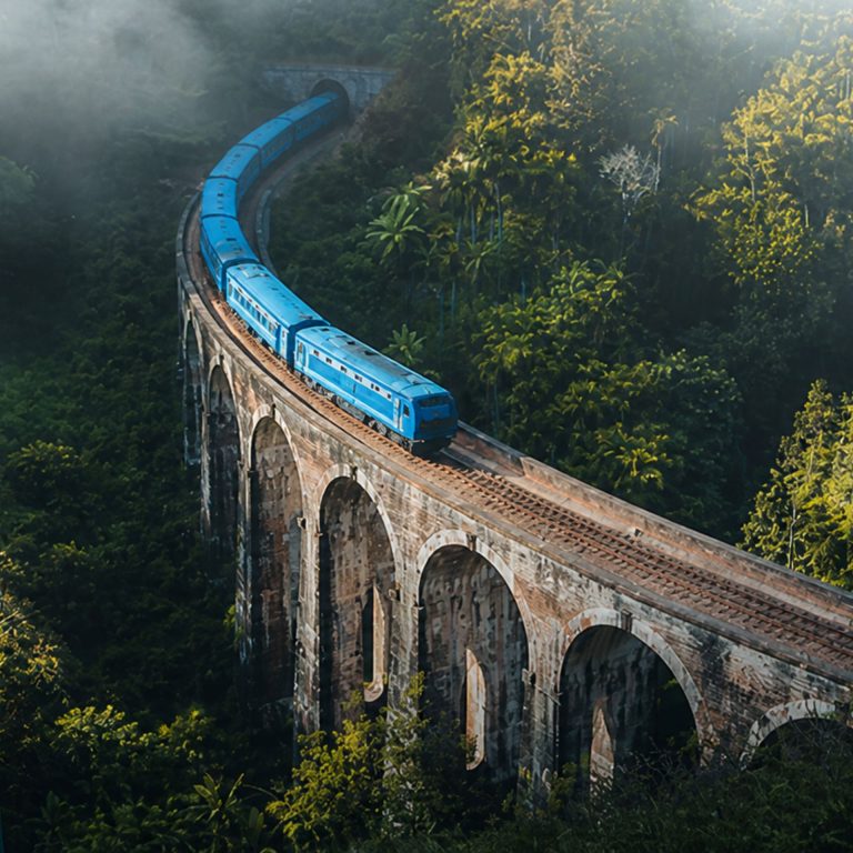 Blauer Zug fährt über die Nine Arch Bridge durch den grünen Dschungel bei Ella in Sri Lanka