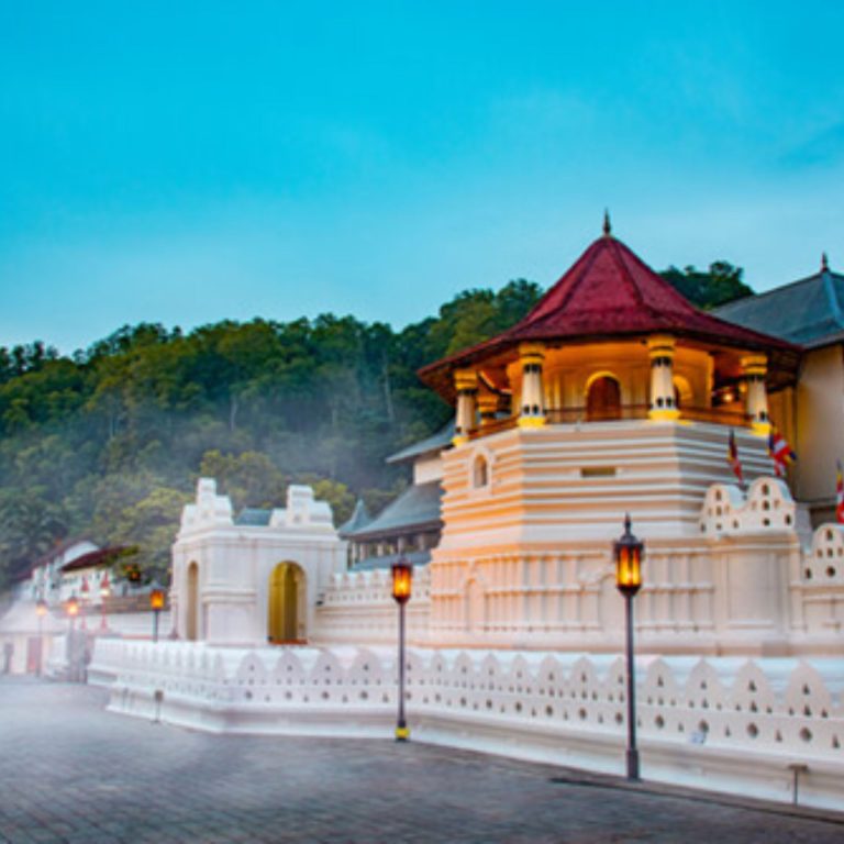 Temple of the Sacred Tooth Relic in Kandy bei Abendlicht mit weißer Tempelmauer und Hügelwald im Hintergrund